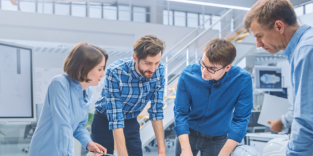 Group of professionals discussing around a table with a large display screen in a bright, modern office.